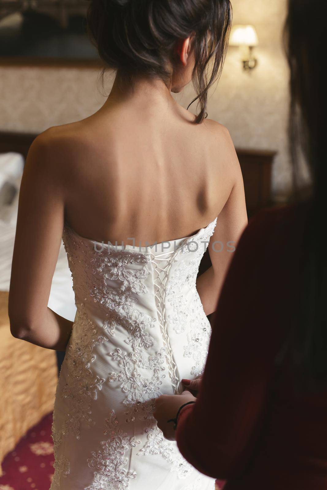 Female hands button the wedding dress to the bride with a beautiful hairstyle. by StudioPeace