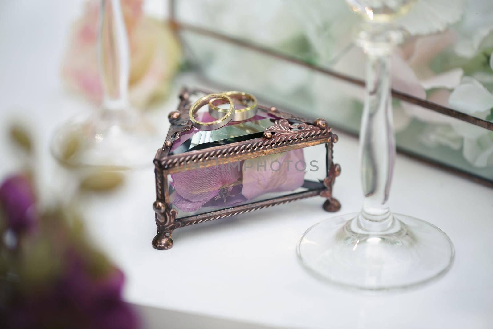 Wedding rings in a glass box with lilac rose petals