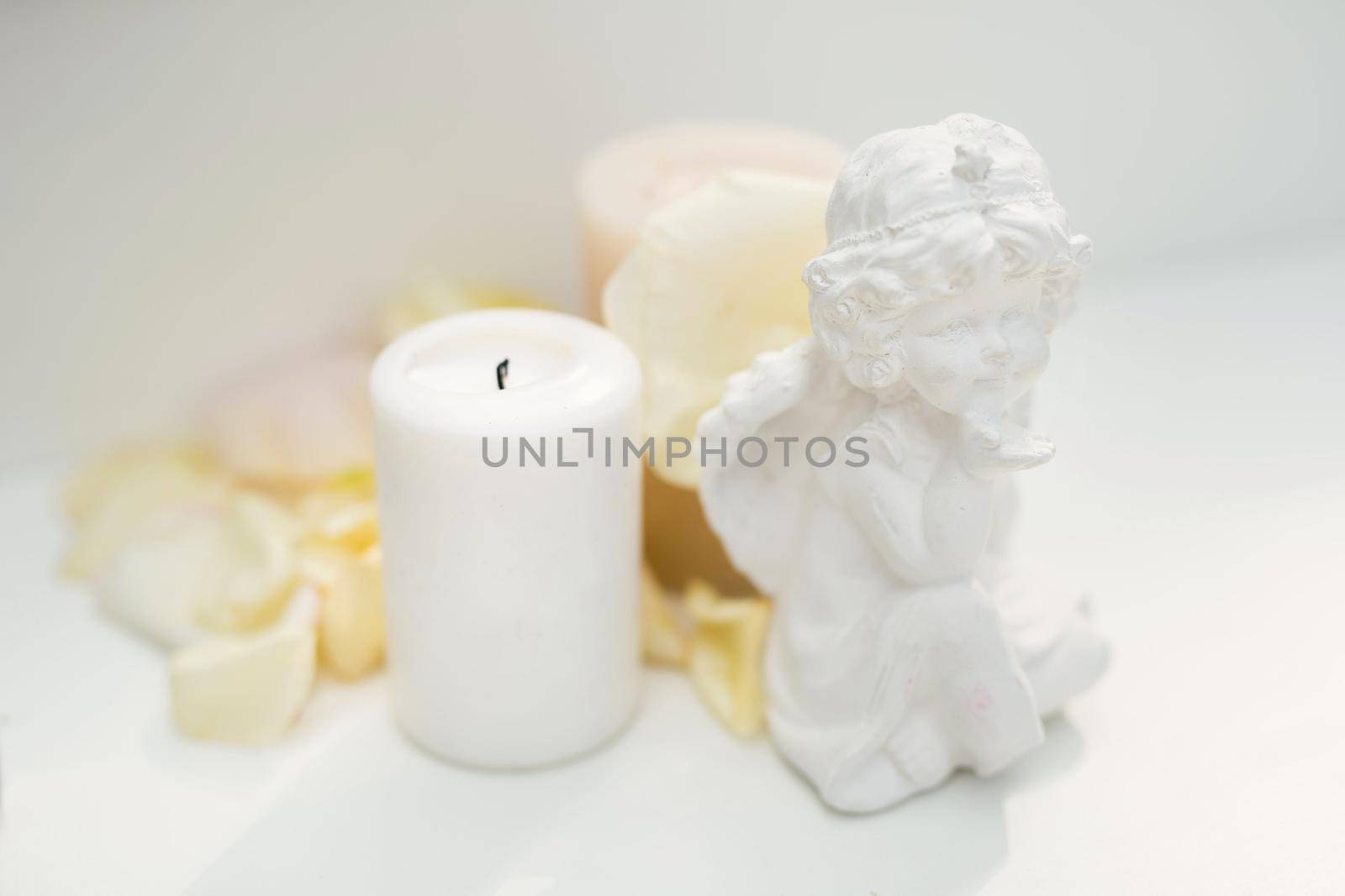 Statuette of an angel, a candle and rose petals on the table.