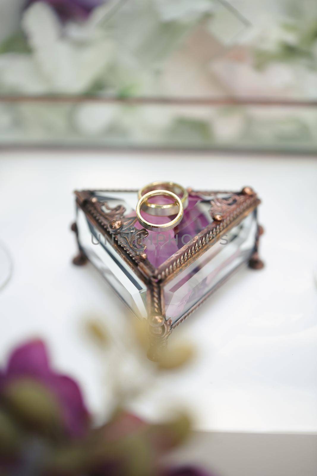 Wedding rings in a glass box with lilac rose petals. by StudioPeace