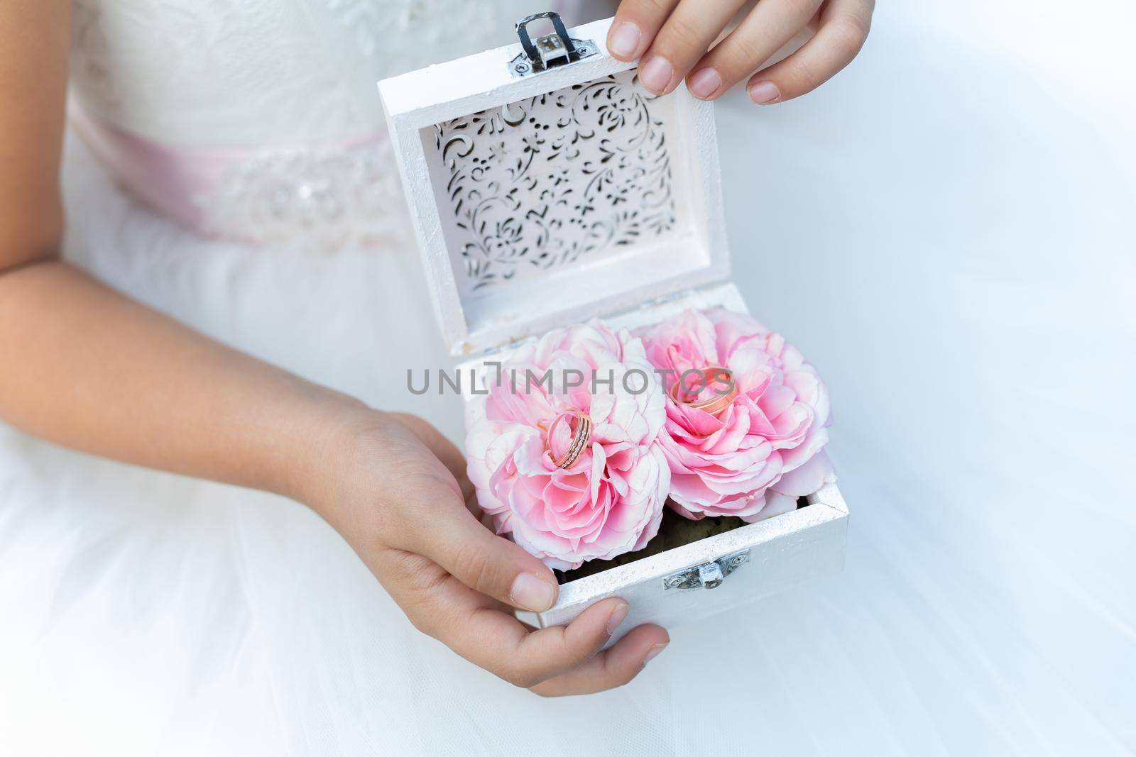 Woman hands holding glass casket with peony flower buds and wedding rings.