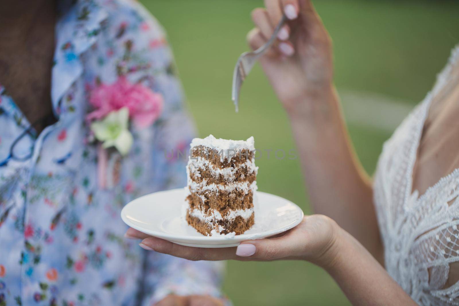 Beautiful young bride feeding wedding cake to groom outdoors. by StudioPeace