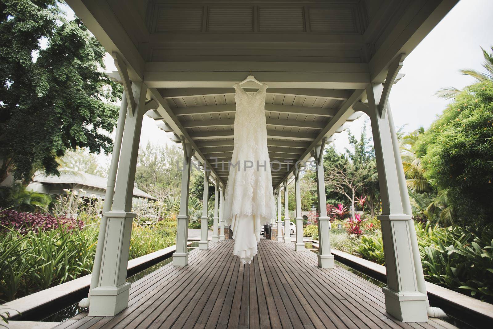 A luxurious wedding dress is hanging in the gazebo on the wedding day by StudioPeace