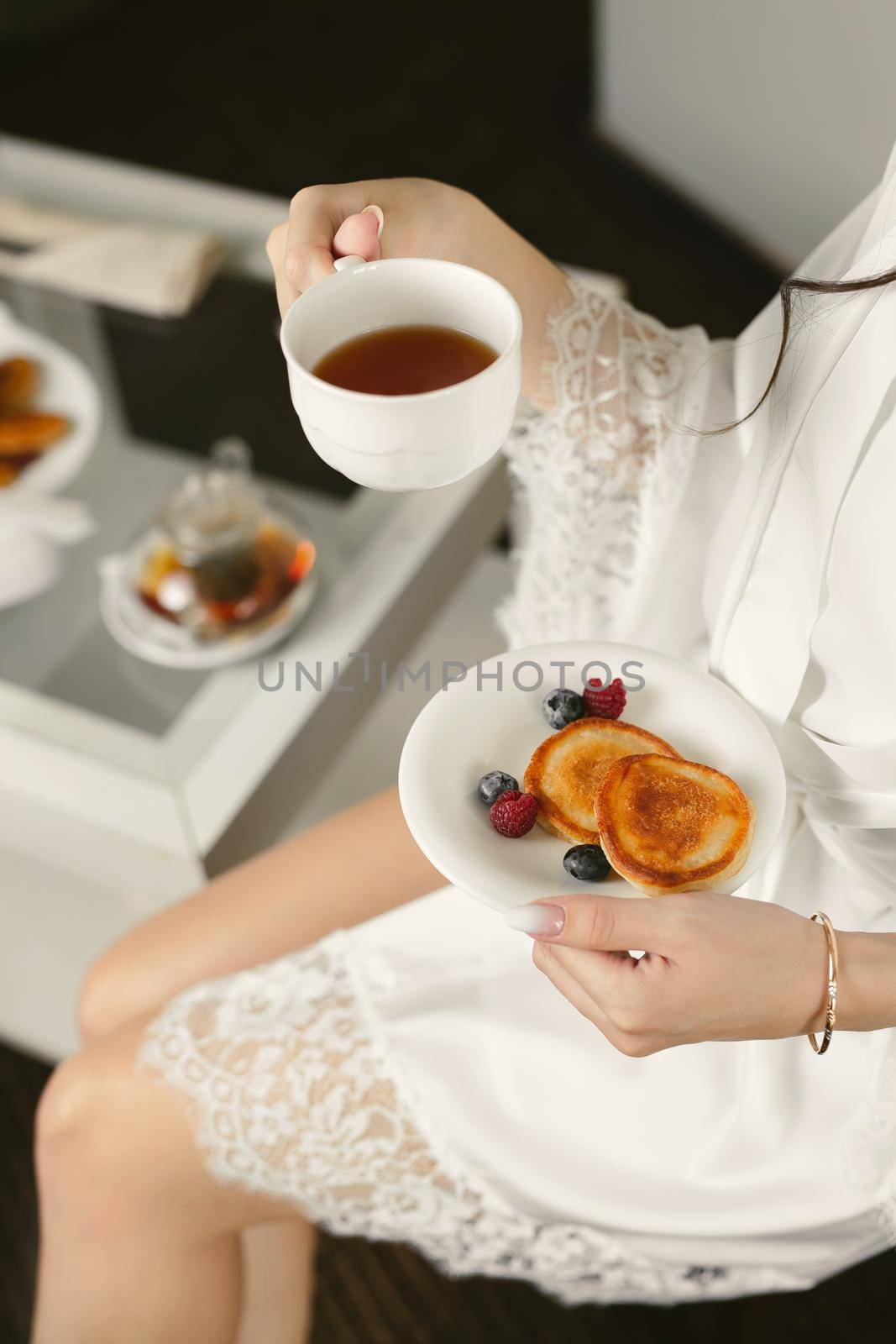Morning of the bride. A woman is holding a mug of tea and pancakes with berries.