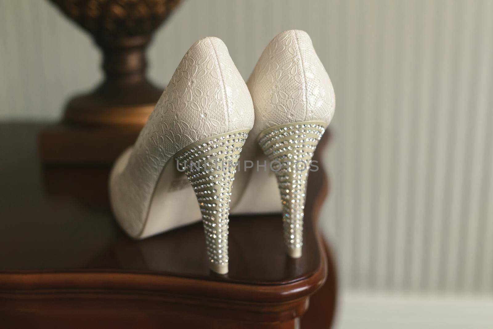 Wedding shoes with heels on a pedestal next to a table lamp by StudioPeace