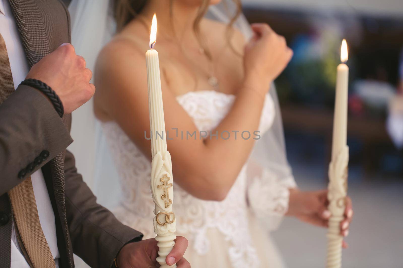 the wedding ceremony in the church. The bride in a white dress and veil holds candles.