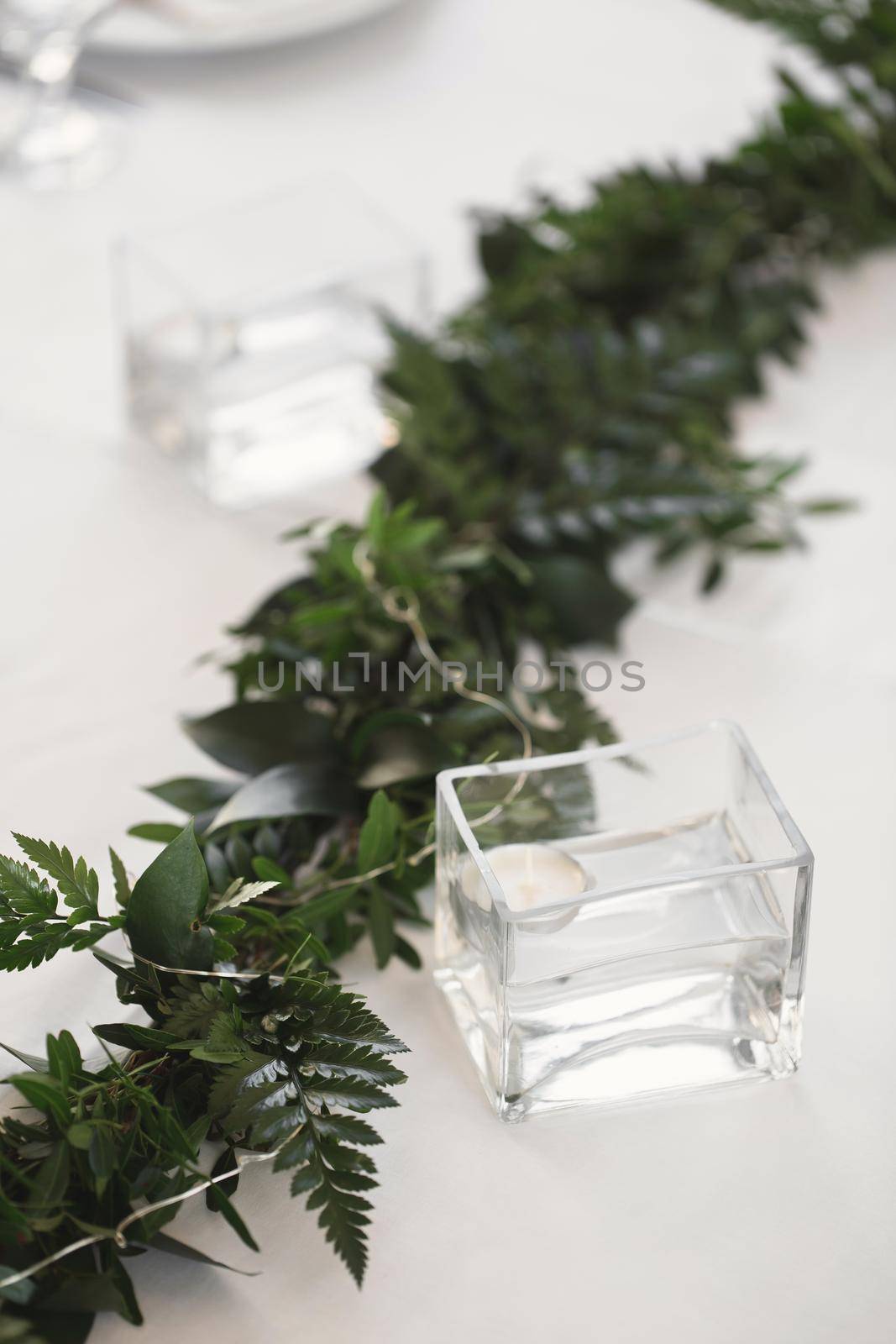 Decor of candles and green flowers on the wedding table in the restaurant by StudioPeace