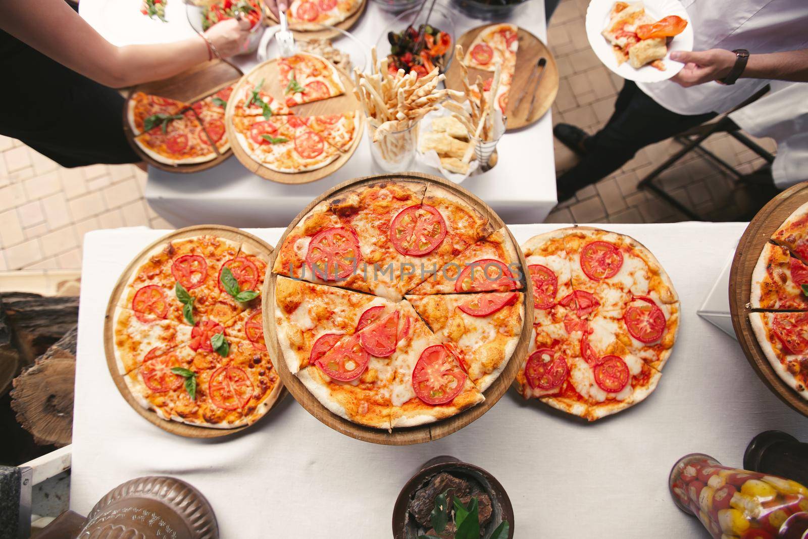 There are many different freshly prepared pizzas on the buffet table by StudioPeace