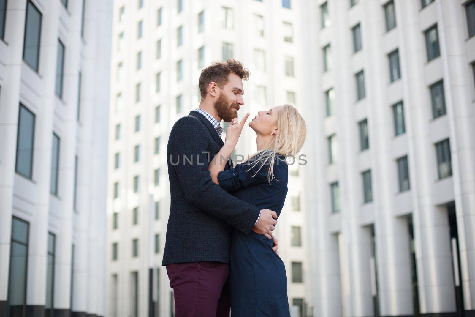 Man and woman hugging and laughing in front of a white building.