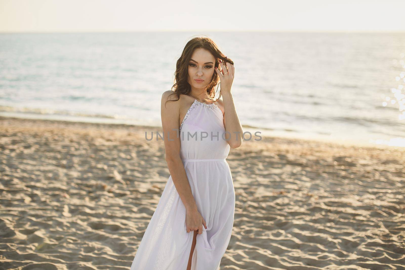 Beautiful girl bride in a white dress and sneakers, at sunset walks along the beach by StudioPeace