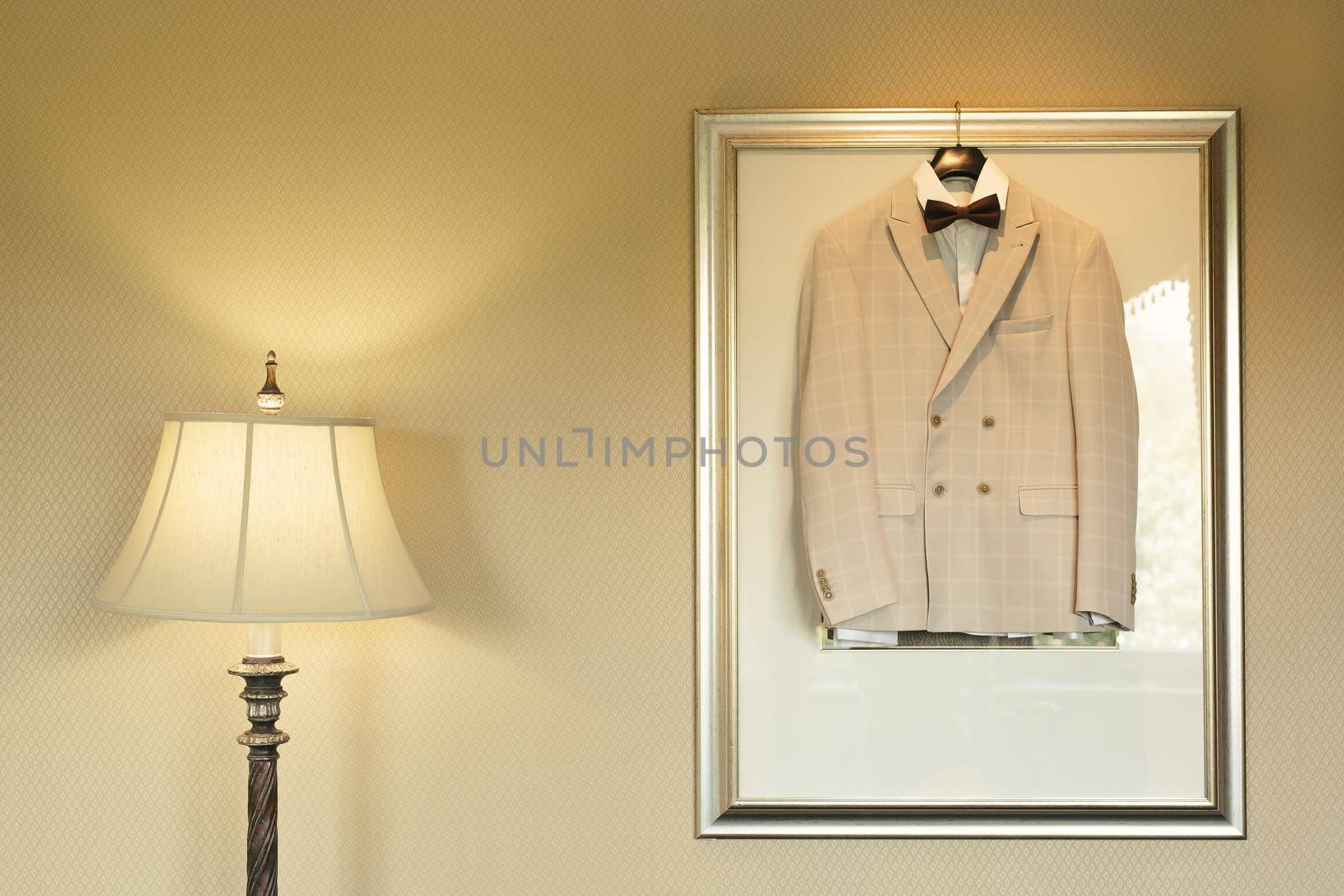 A light festive wedding jacket hangs on a wall lamp in a room with a table lamp by StudioPeace