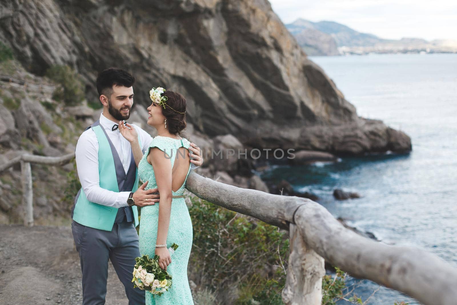 The bride and groom on nature in the mountains near the water. Suit and dress color Tiffany. Kiss and hug by StudioPeace