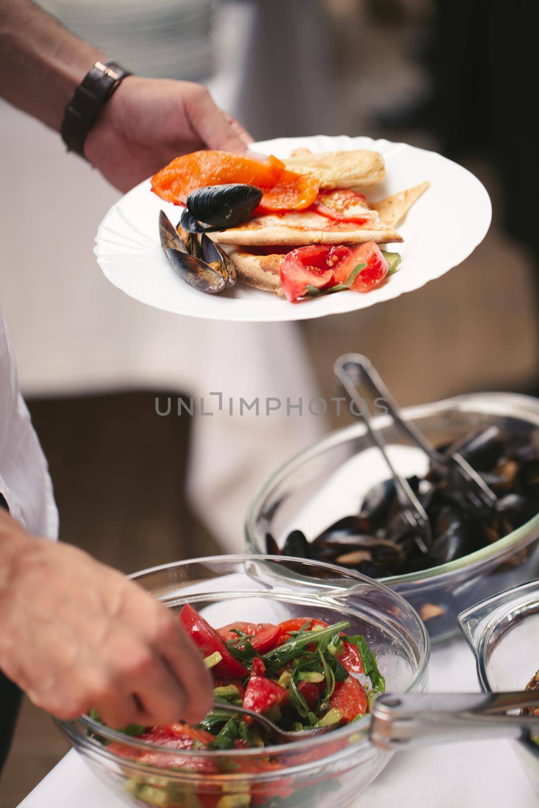 A man's hands put sea products on a plate at a buffet.