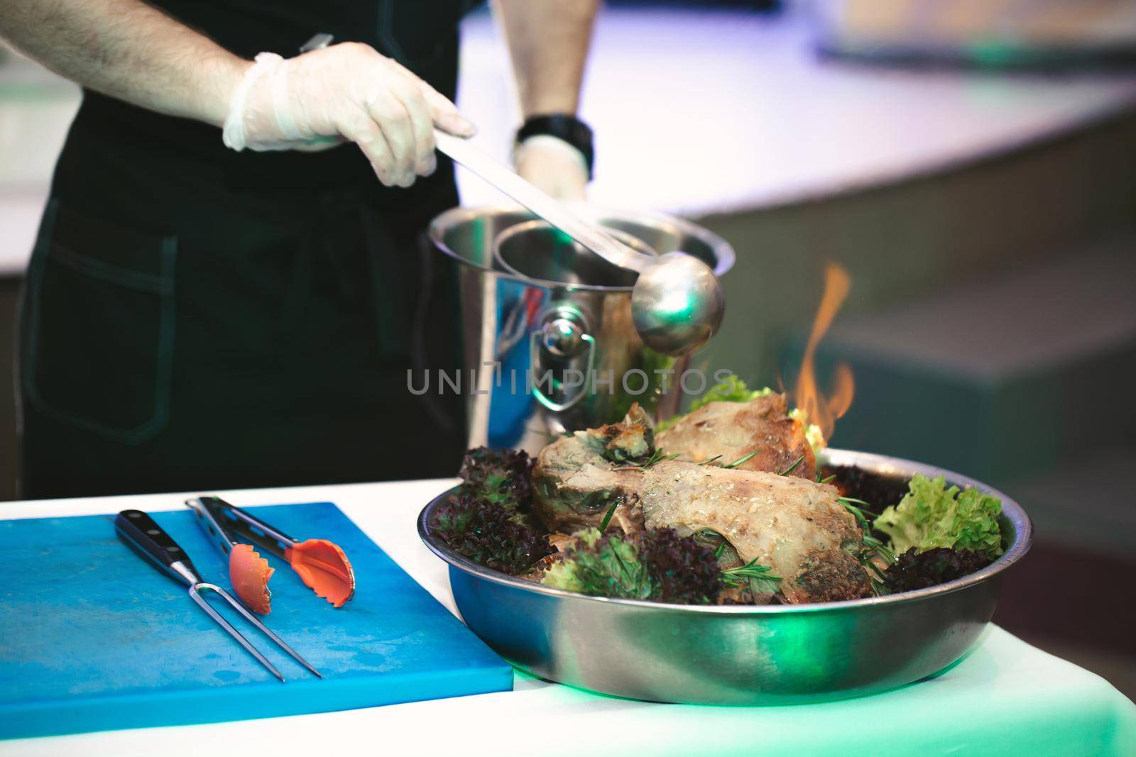 The chef's hands pour broth over the meat in the process of cooking flambe by StudioPeace