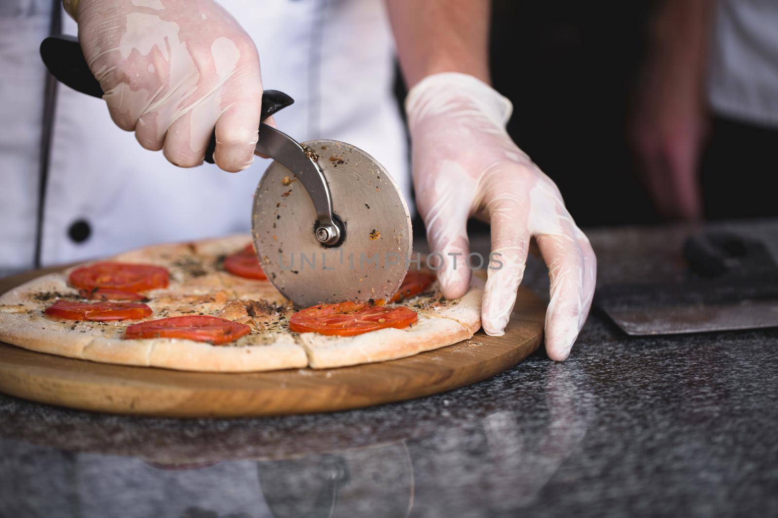 The cook cuts pizza with a round knife.