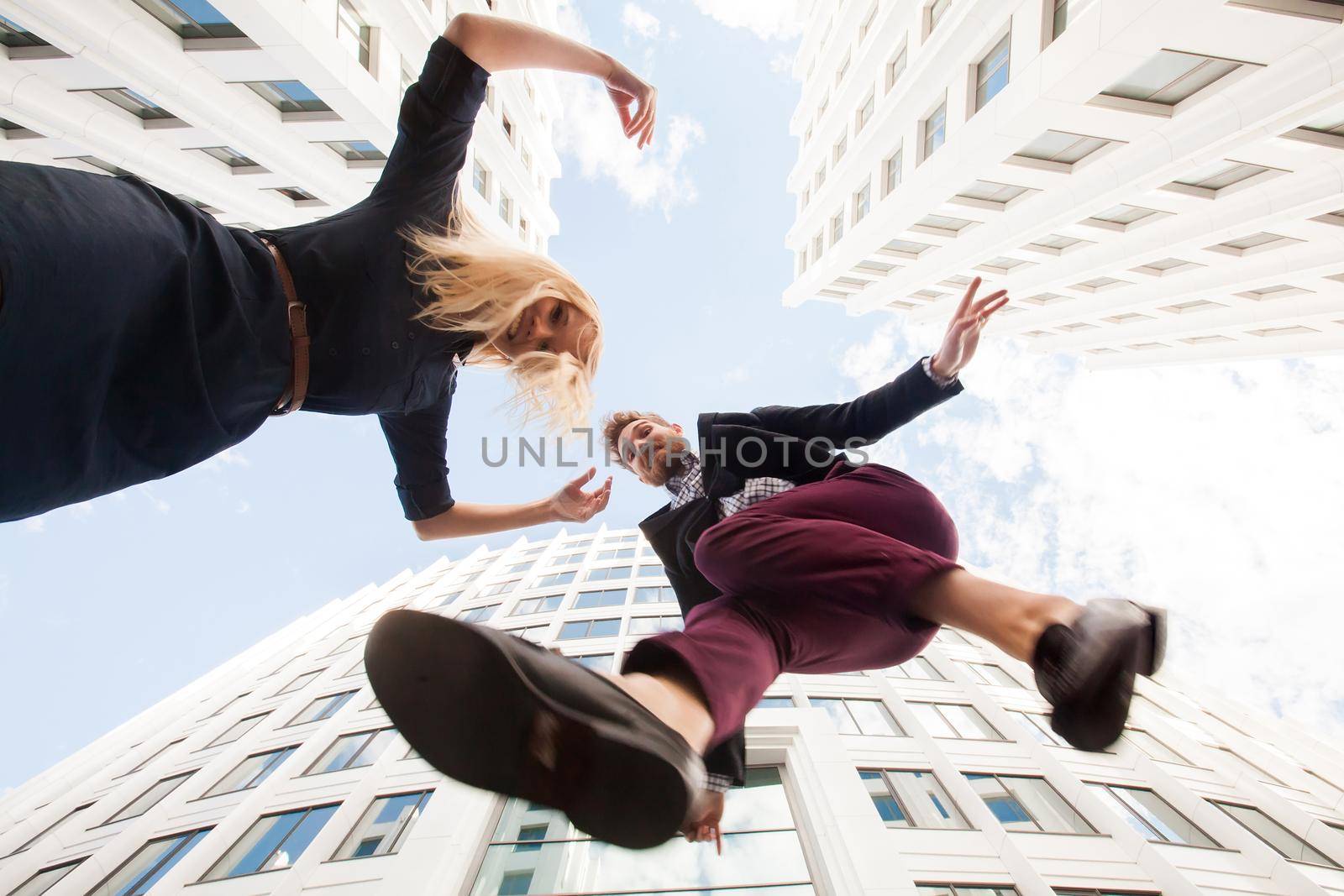 Cheerful young couple fooling around, jumping on the background of the building. Bottom view. by StudioPeace
