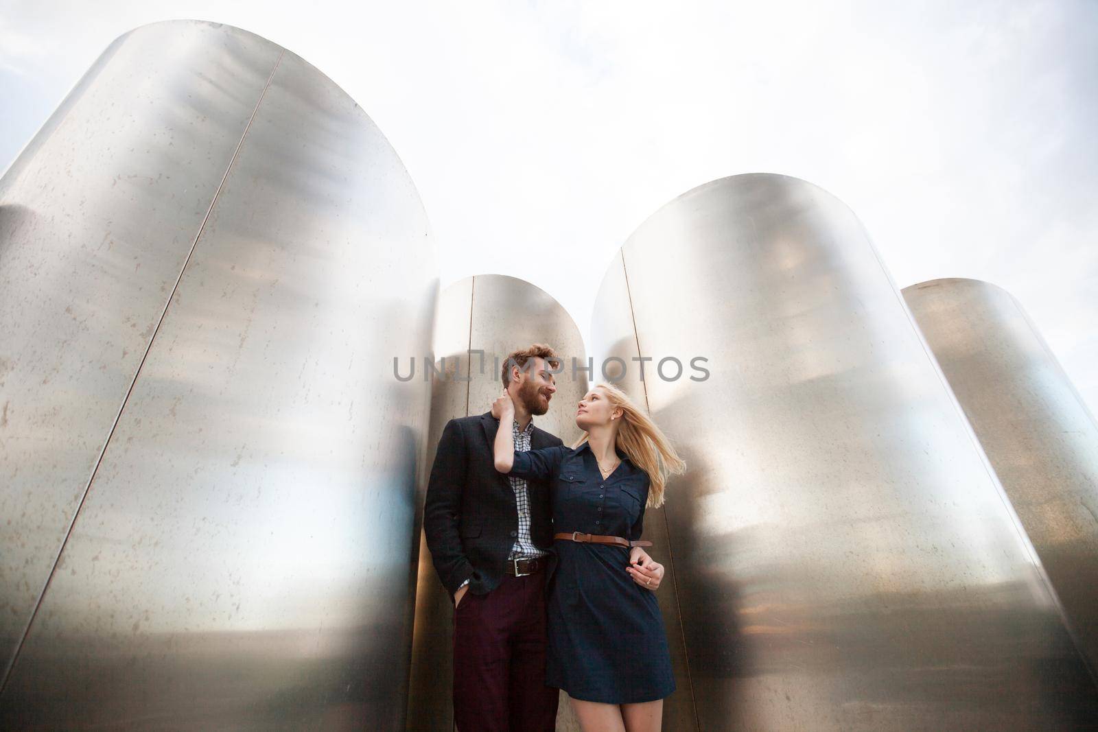 Man and woman pose in front of the large metal pipes. by StudioPeace