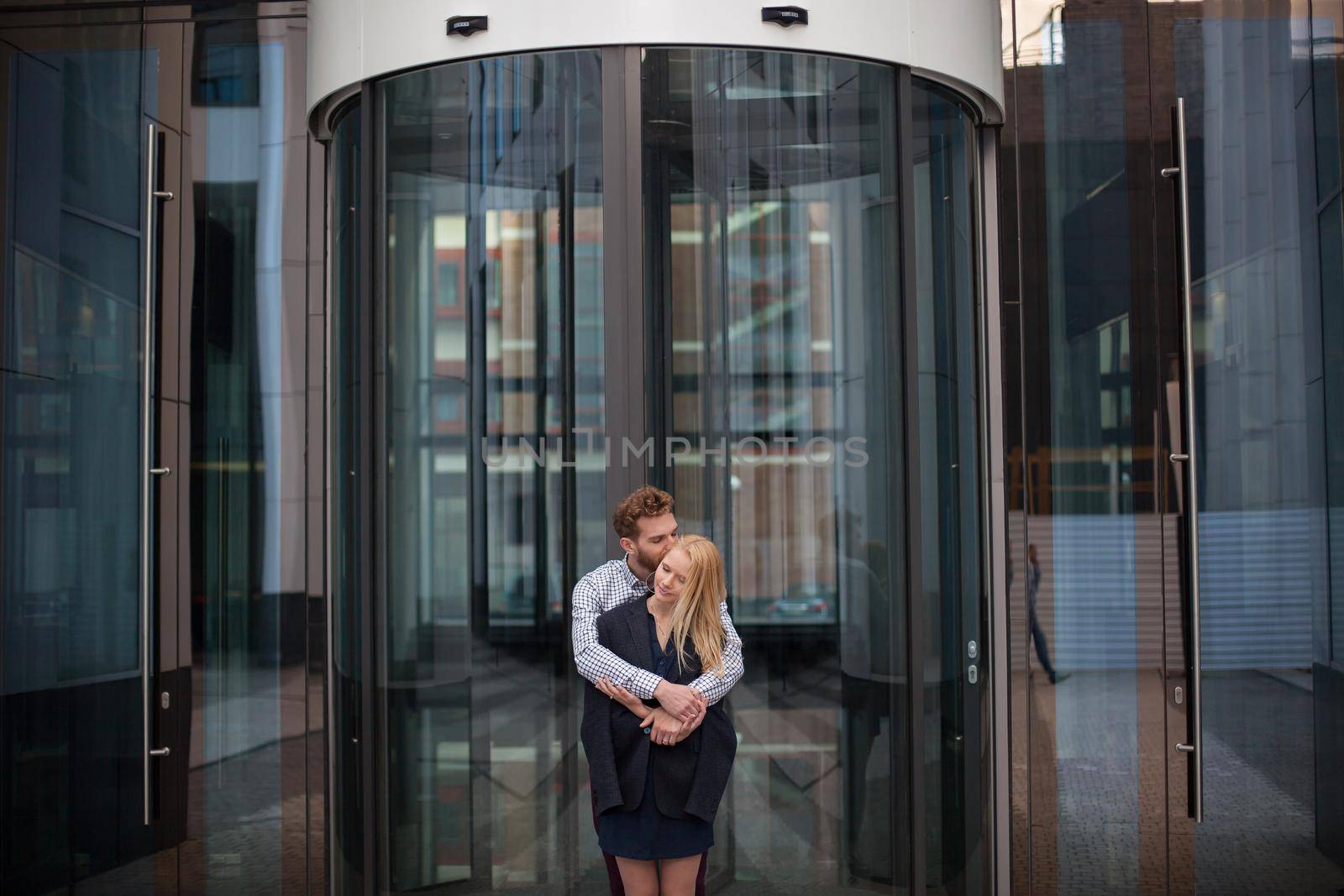 A man hugs a woman in the background of the glass building by StudioPeace