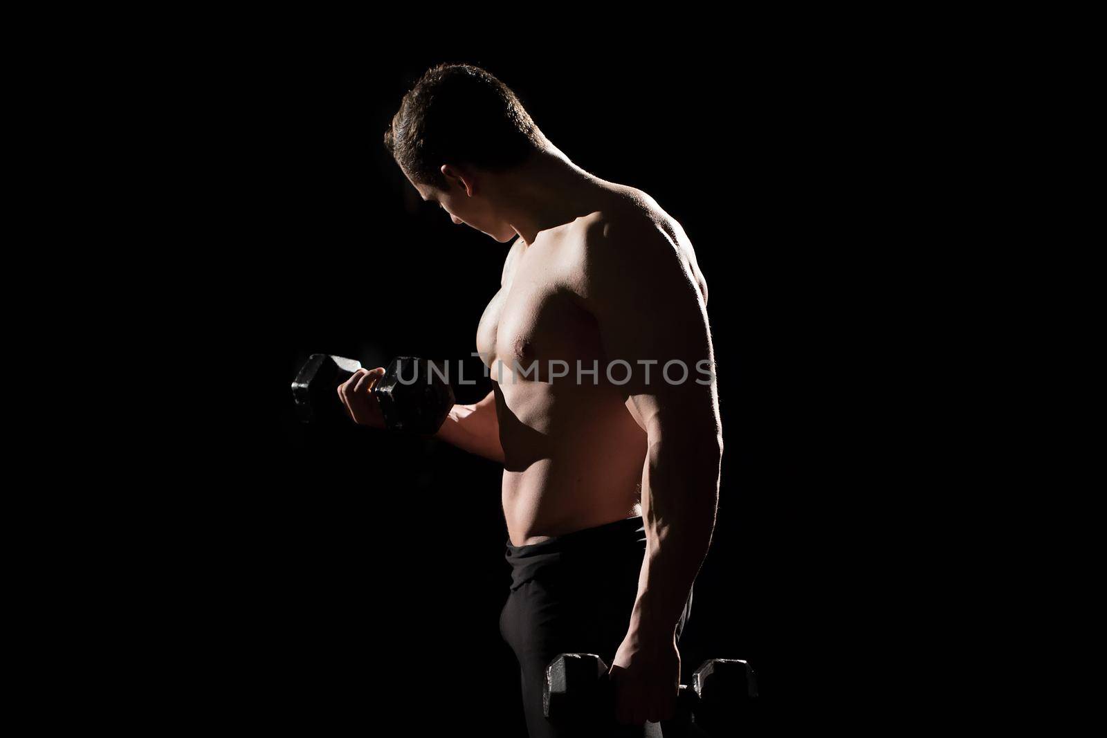 Handsome power athletic guy bodybuilder doing exercises with dumbbell. Fitness muscular body on dark background by StudioPeace