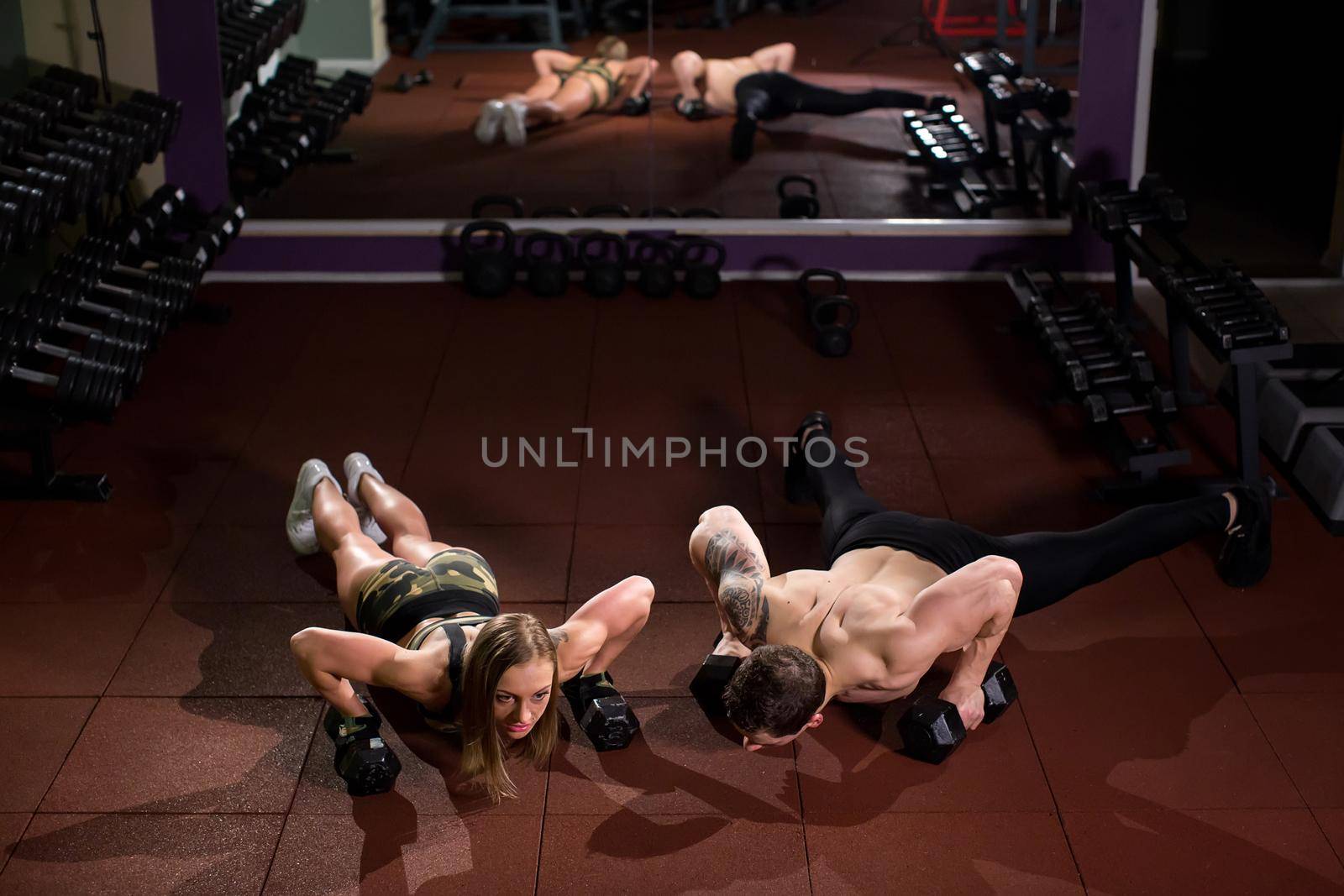 Gym man and woman push-up strength pushup with dumbbell in a fitness workout. by StudioPeace