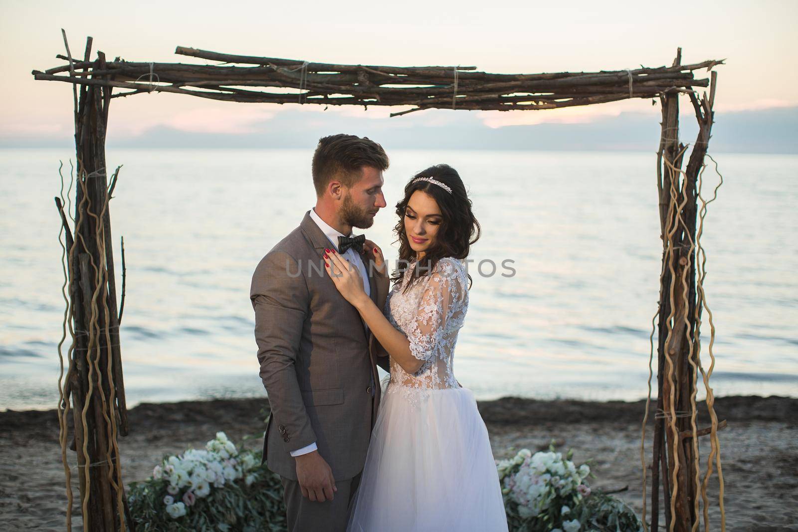 The bride and groom under archway on beach. Sunset, twilight by StudioPeace