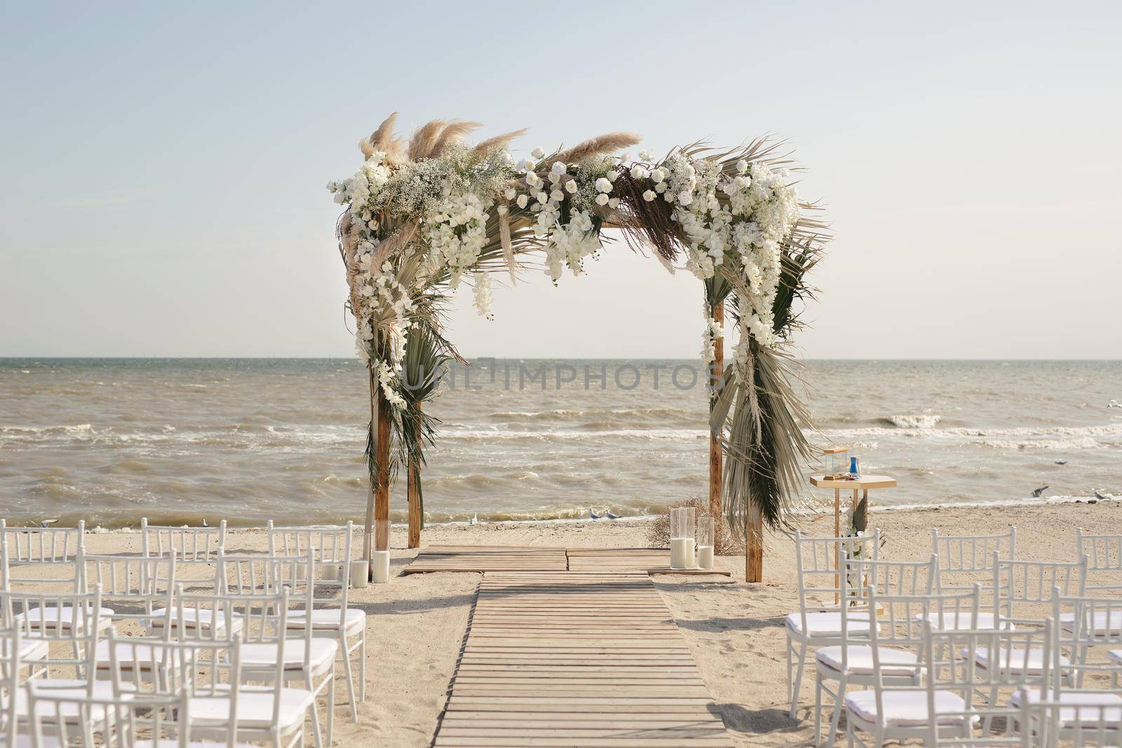 Outdoor area for beach ceremonies with sea view, white chairs, flower arch on a sunny day. by StudioPeace