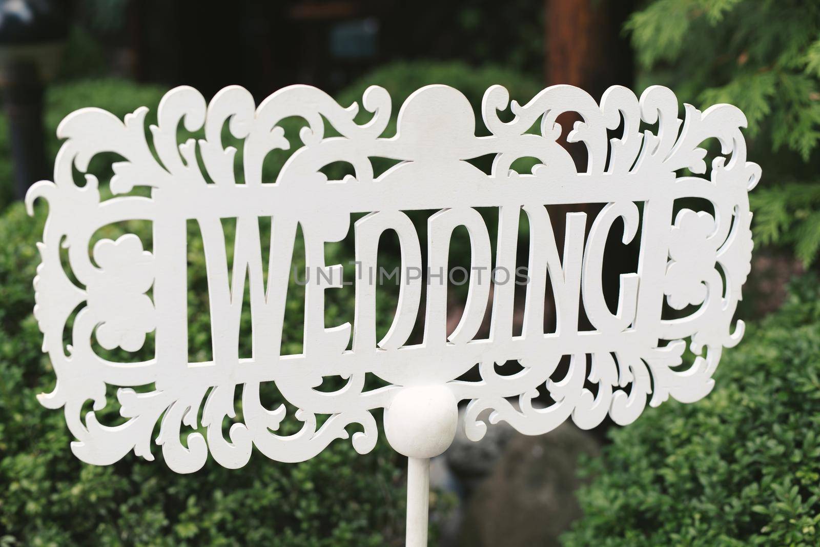 White wooden sign in the form of an arrow and a pointer with the inscription and letters - wedding in English stands in nature at the ceremony by StudioPeace
