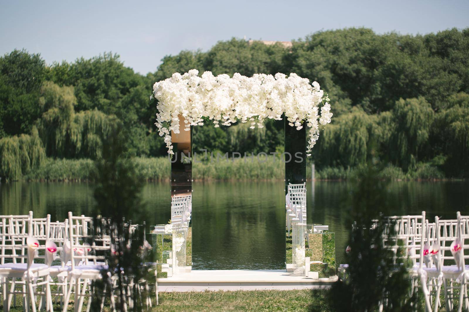 White mirrored wedding arch decorated with white flowers. The concept of an outdoor wedding ceremony venue.
