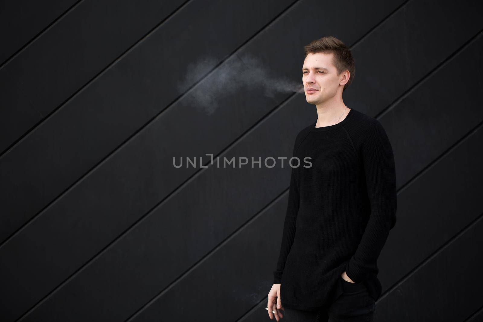 Young handsome guy Smoking a cigarette on black background. by StudioPeace