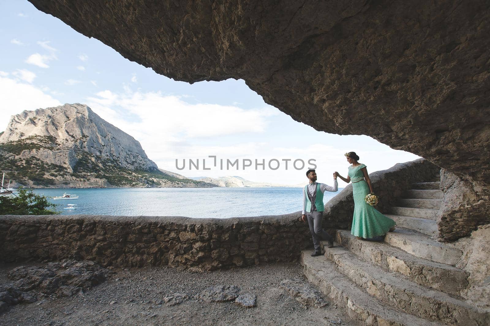 The bride and groom on nature in the mountains near the water. Suit and dress color Tiffany. Walk hand in hand.