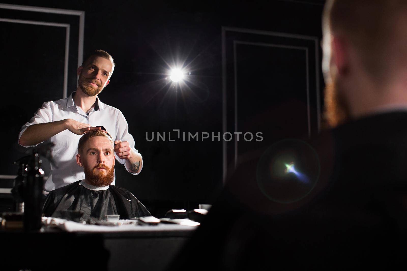 Master cuts hair and beard in the Barber shop. Hairdresser makes hairstyle using scissors and a metal comb by StudioPeace