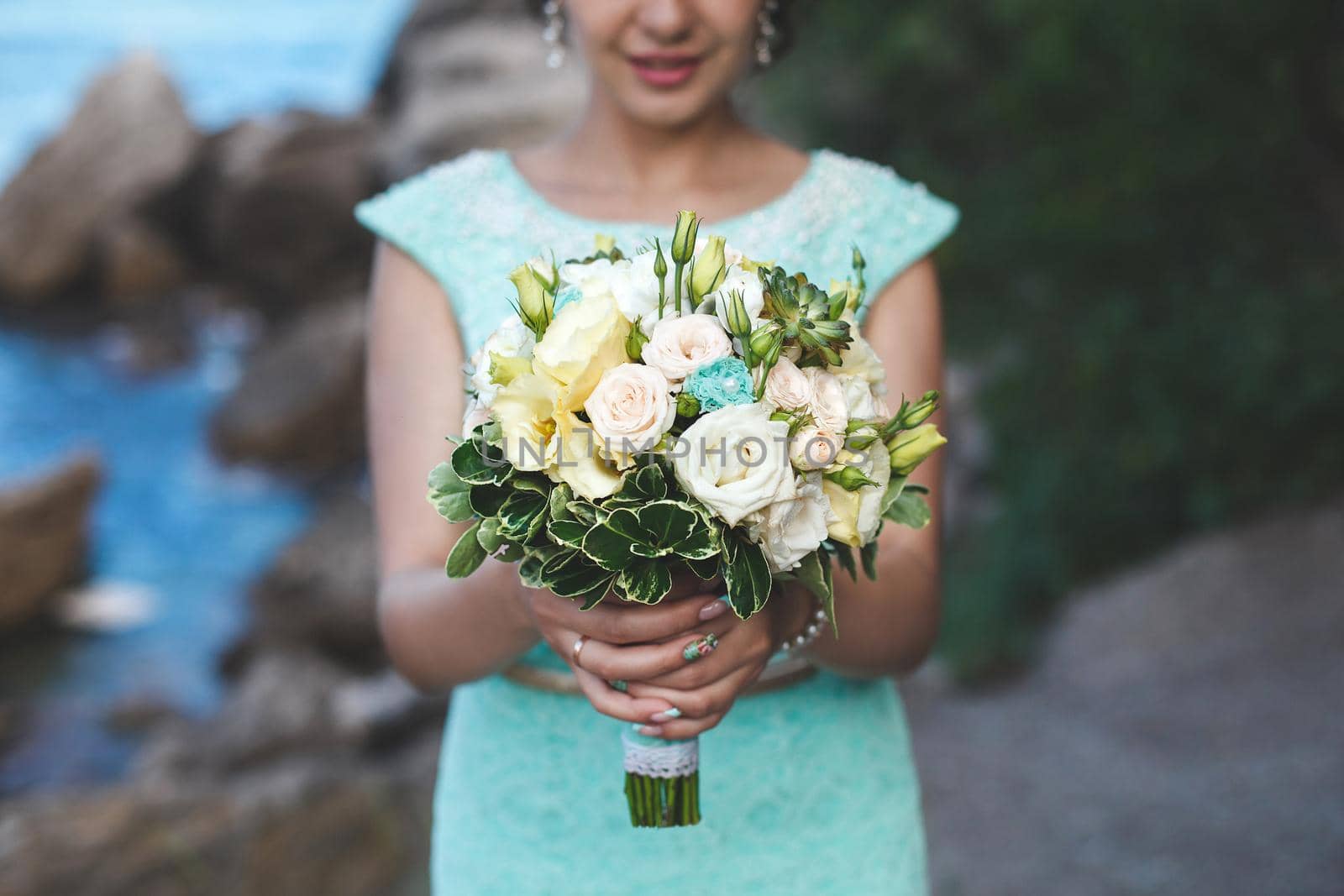 Bride in nature in the mountains near the water. Dress color Tiffany. Bride posing with bouquet.