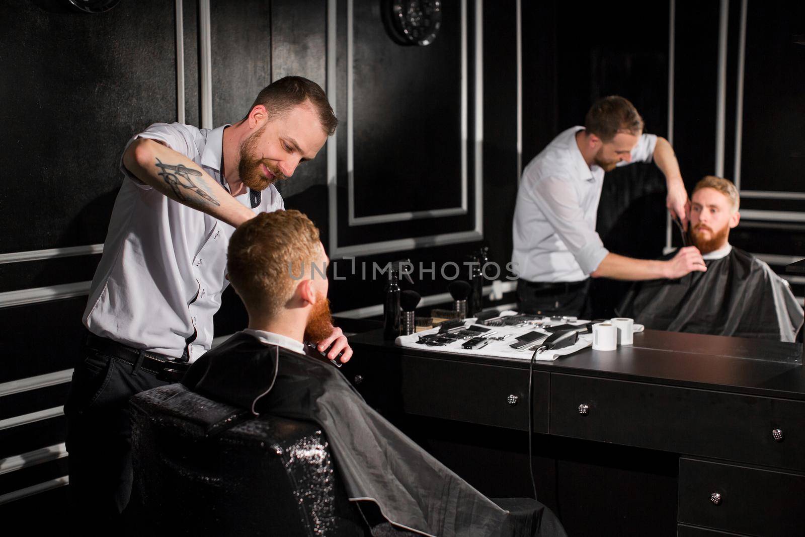 Master cuts hair and beard in the Barber shop. Hairdresser makes hairstyle using scissors and a metal comb by StudioPeace