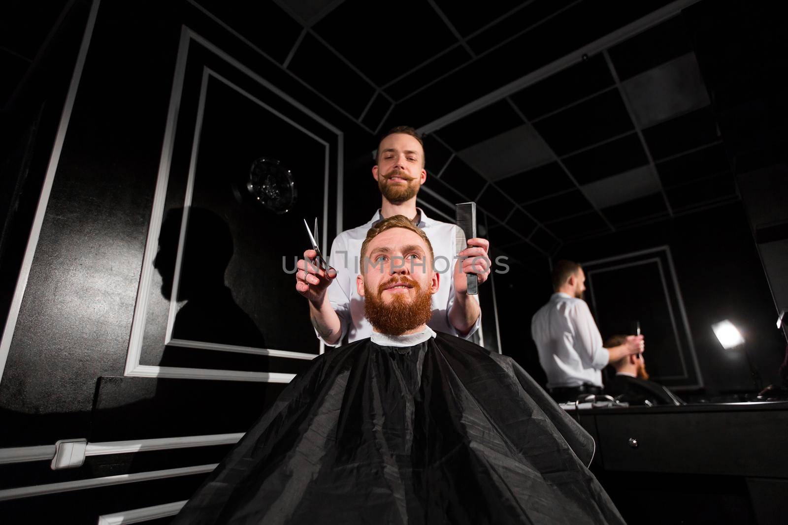 Master cuts hair and beard in the Barber shop. Hairdresser makes hairstyle using scissors and a metal comb