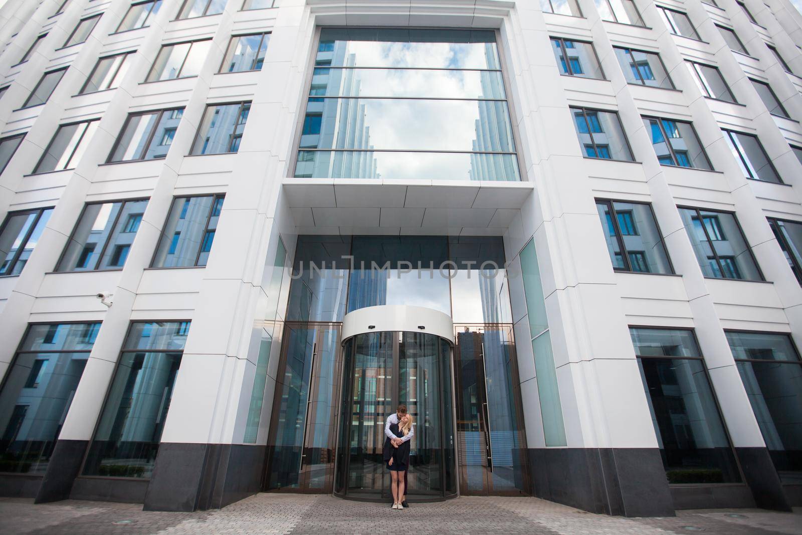 A man hugs a woman in the background of the glass building by StudioPeace