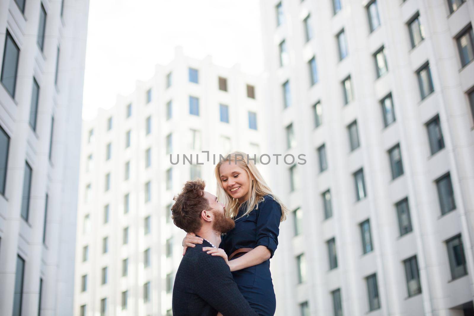 Man and woman hugging and laughing in front of a white building.