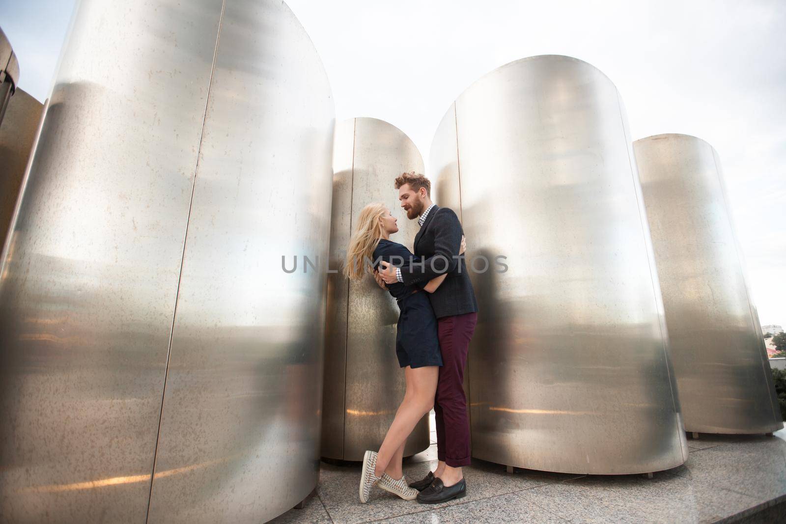 Man and woman pose in front of the large metal pipes. by StudioPeace