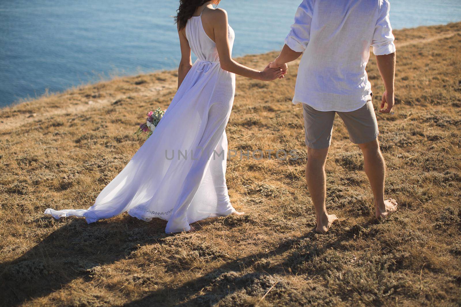Beautiful young couple walks along the ocean at sunset by StudioPeace