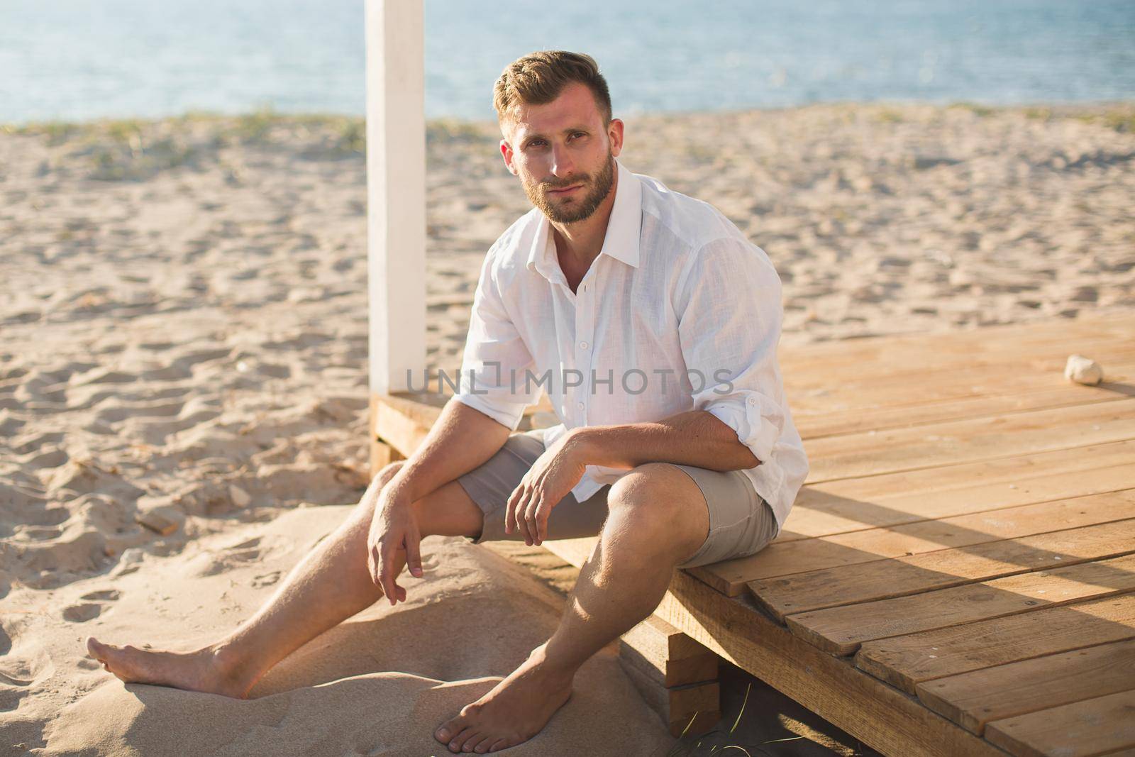 The man in the white shirt and shorts sitting on the beach by StudioPeace