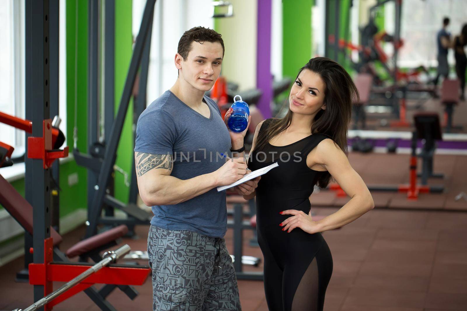Handsome muscled male trainer consulting attractive young female in gym, both smiling. by StudioPeace