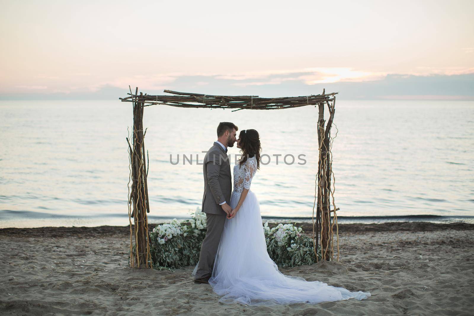 The bride and groom under archway on beach. Sunset, twilight.
