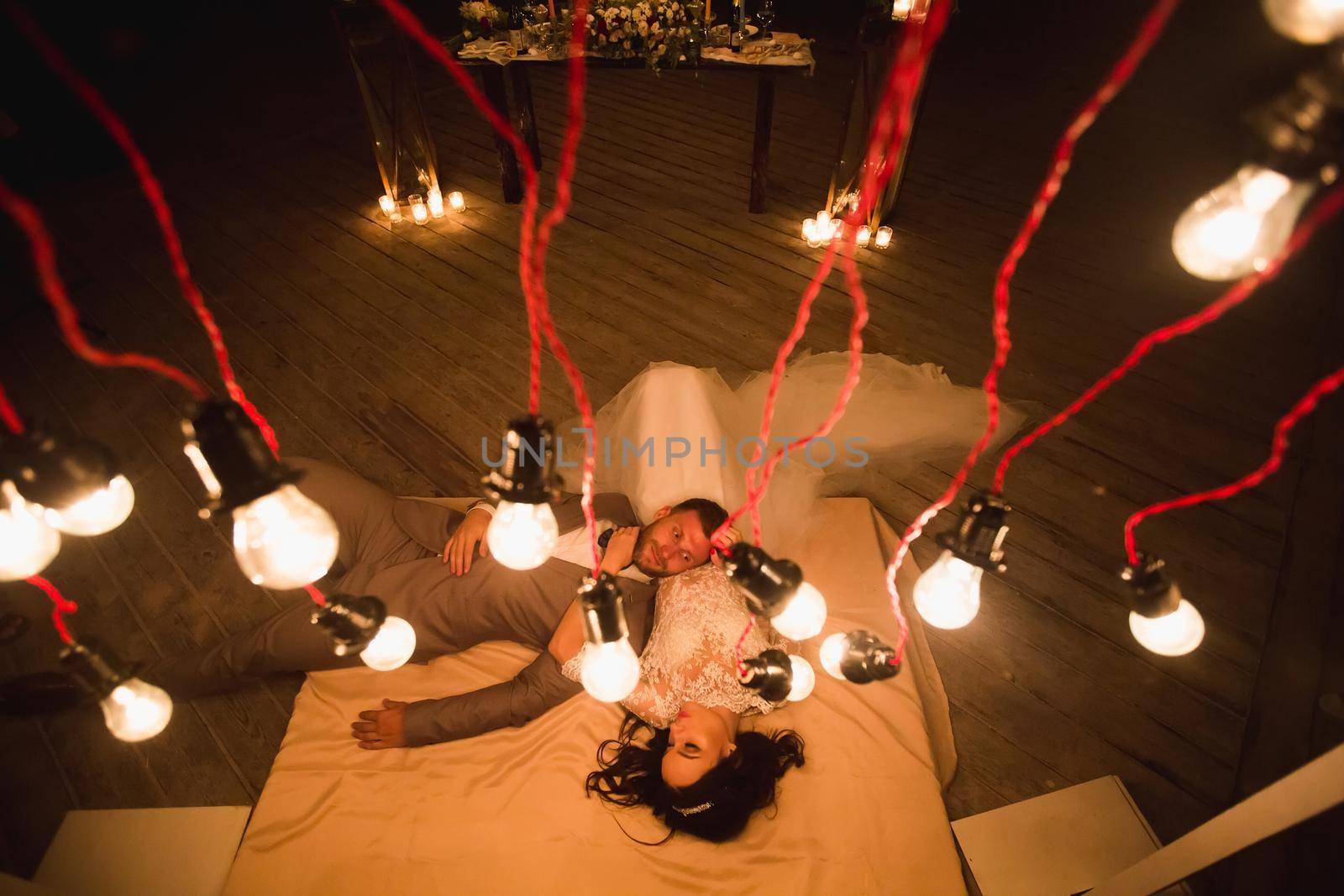 The night wedding ceremony. The bride and groom are lying on the bed. by StudioPeace