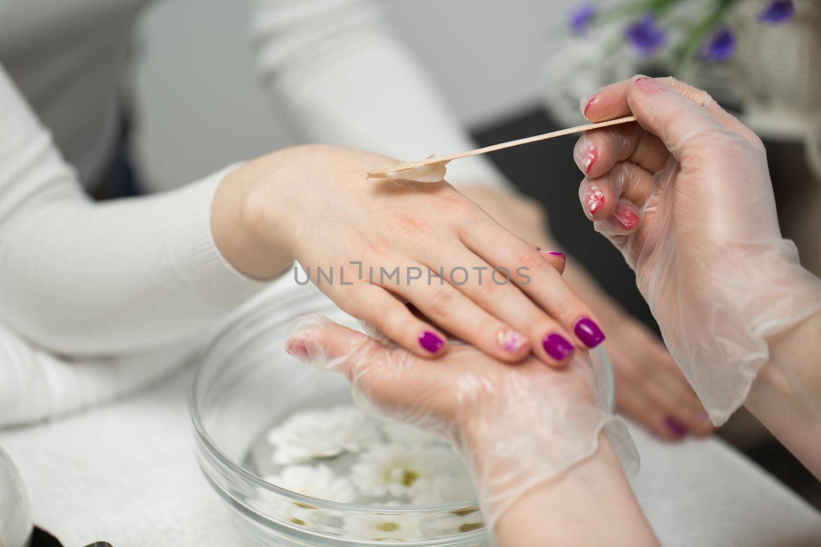Woman in a nail salon receiving a manicure, she is bathing her hands in paraffin or wax. by StudioPeace