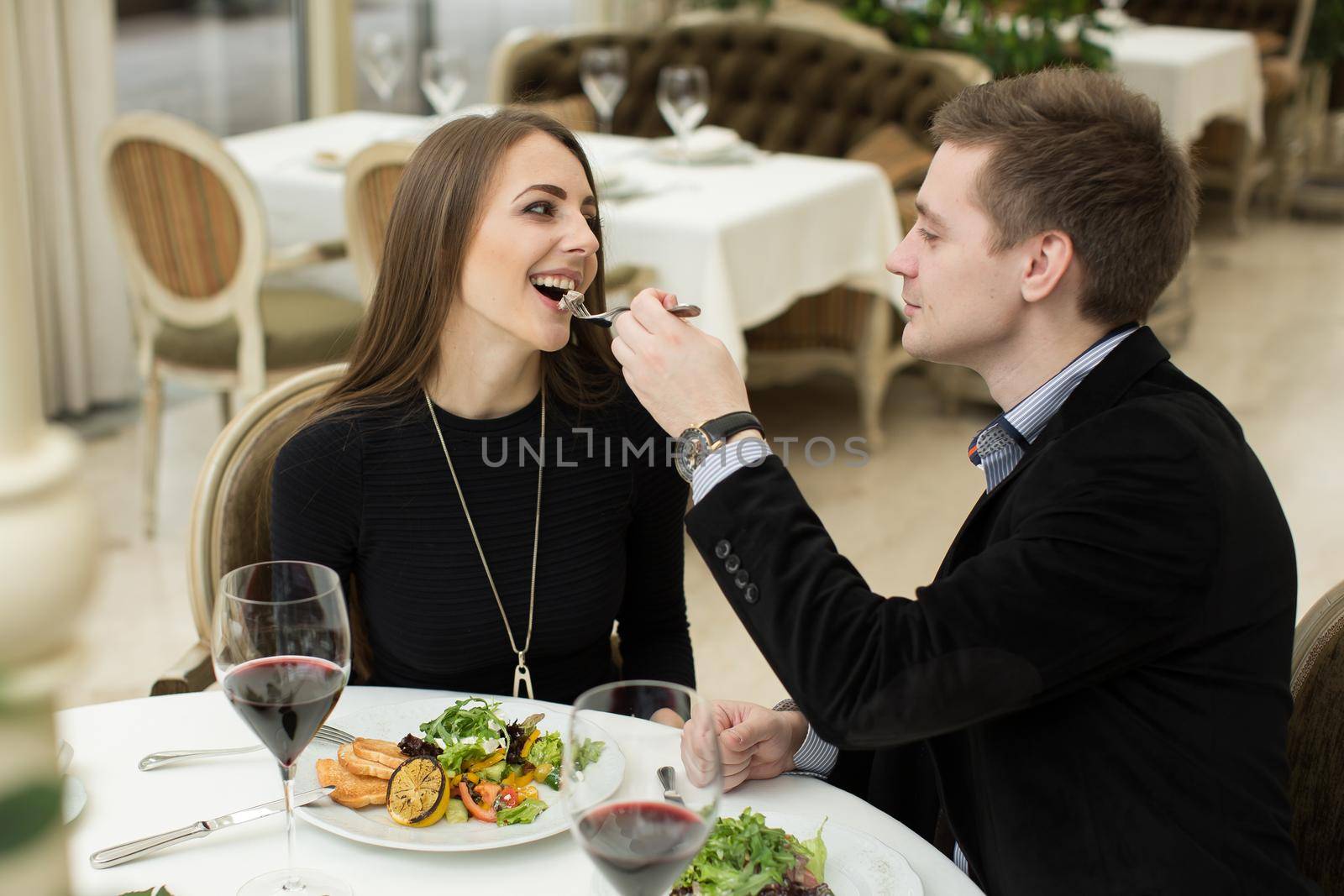 Beautiful young couple feeding each other and smiling while spending time at the restaurant. by StudioPeace