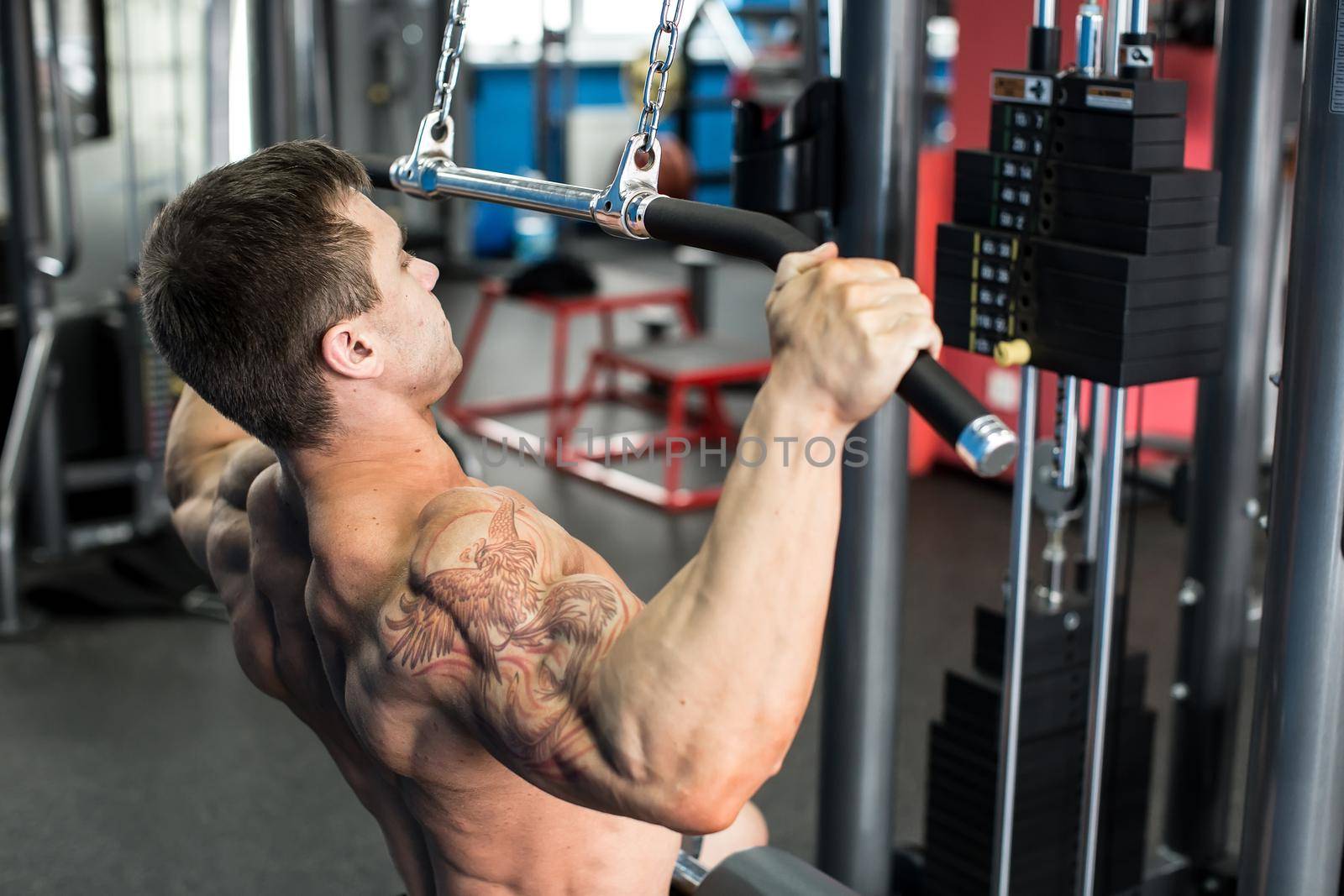 Shoulder pull down machine. Fitness man working out lat pulldown training at gym. Upper body strength exercise for the upper back.