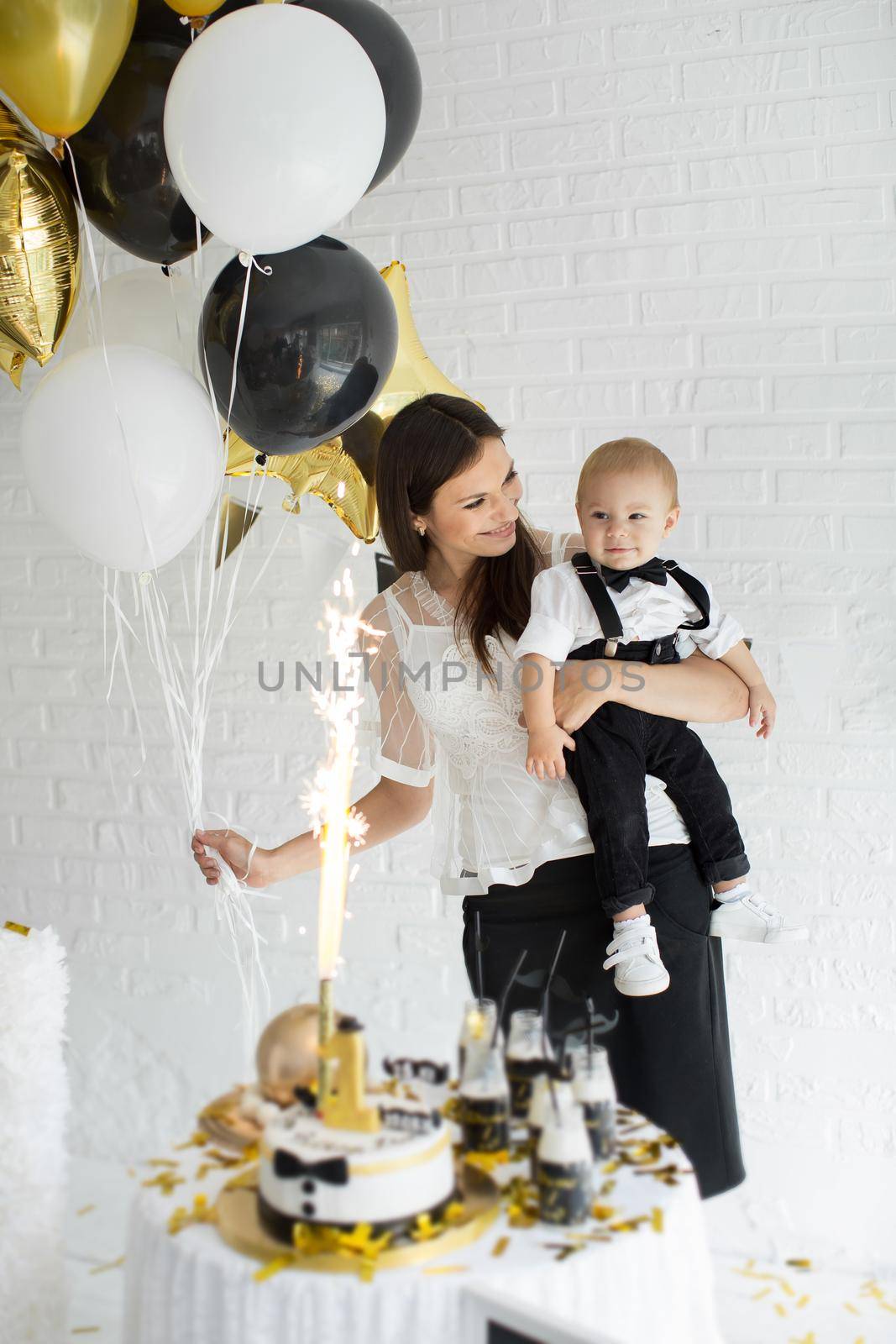 Mother and son celebrating the 1st birthday together laughing and smiling with balloons, a candy bar.