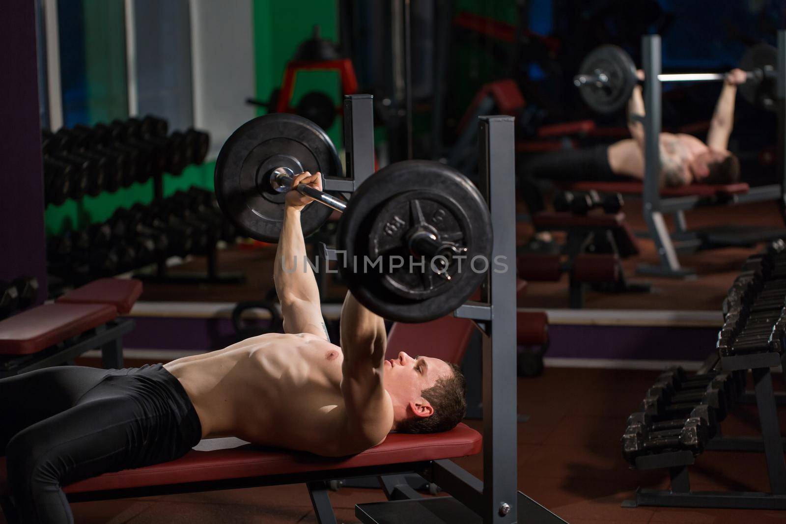 Brutal athletic man pumping up muscles on bench press