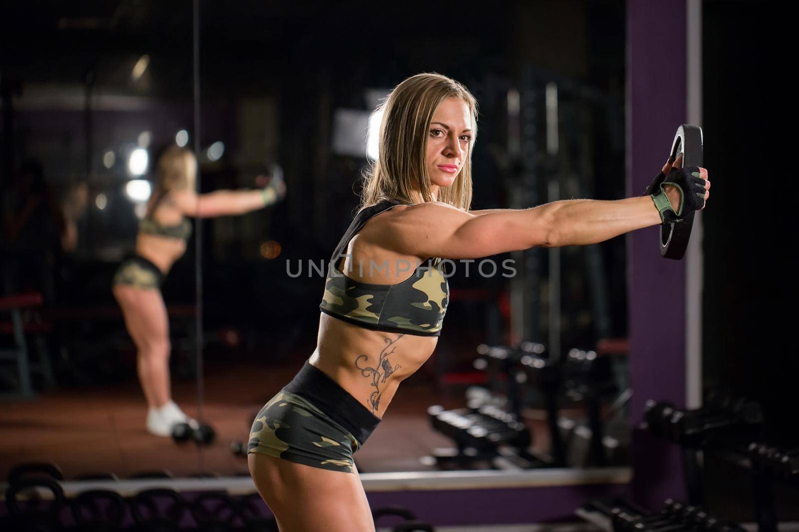 Beautiful bodybuilder woman with lifting dumbbells. Sporty girl showing her well trained body. Well-developed muscles by strength training.