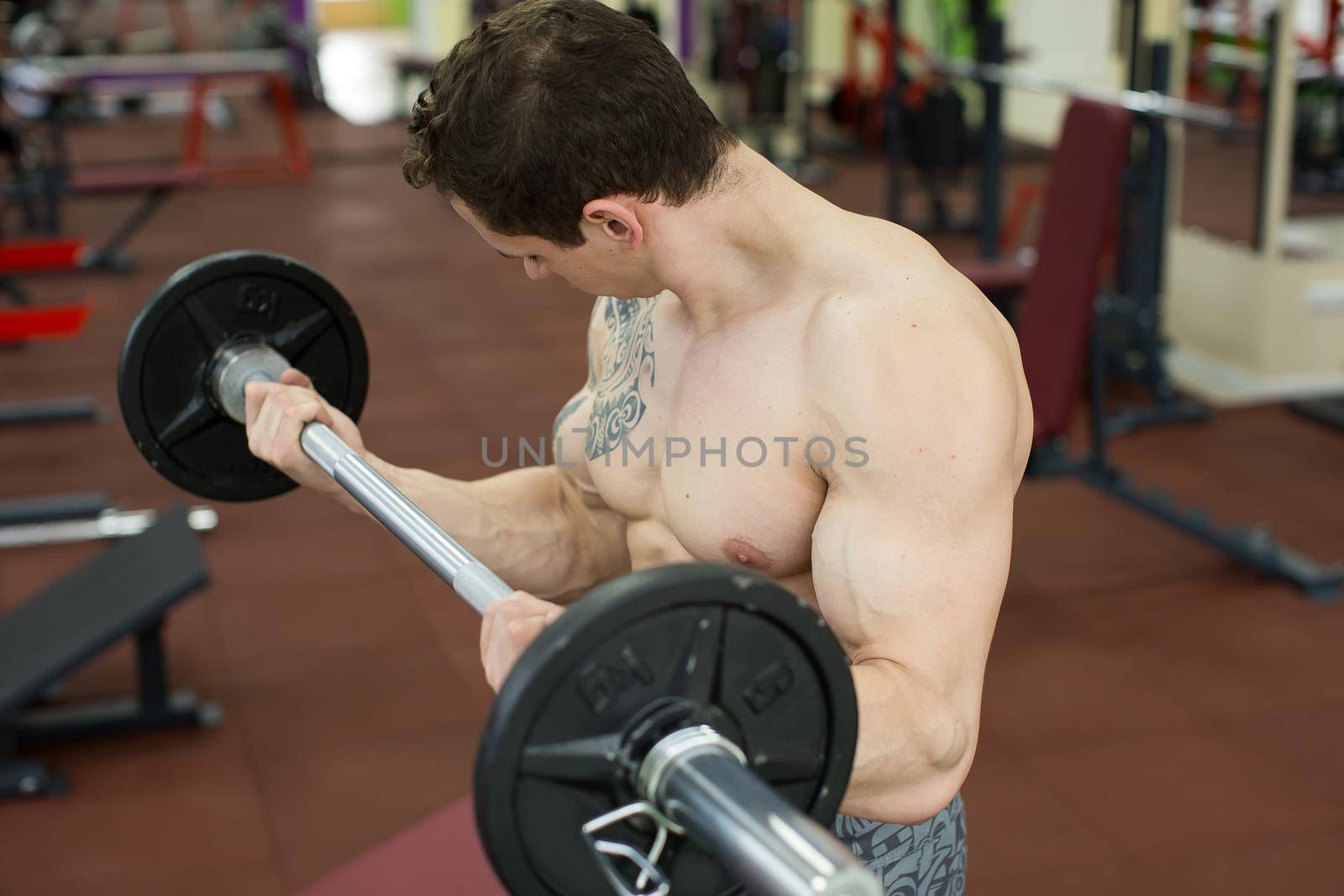 Muscular man working out in gym doing exercises with barbell, strong male naked torso abs