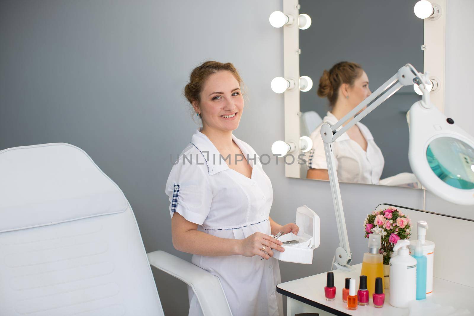 Manicure in a white robe holding in his hands the instruments in the beauty salon.